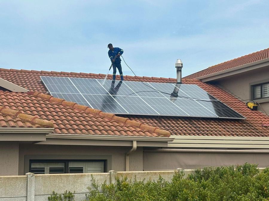 Worker on a tiled roof washing a bank of solar panels